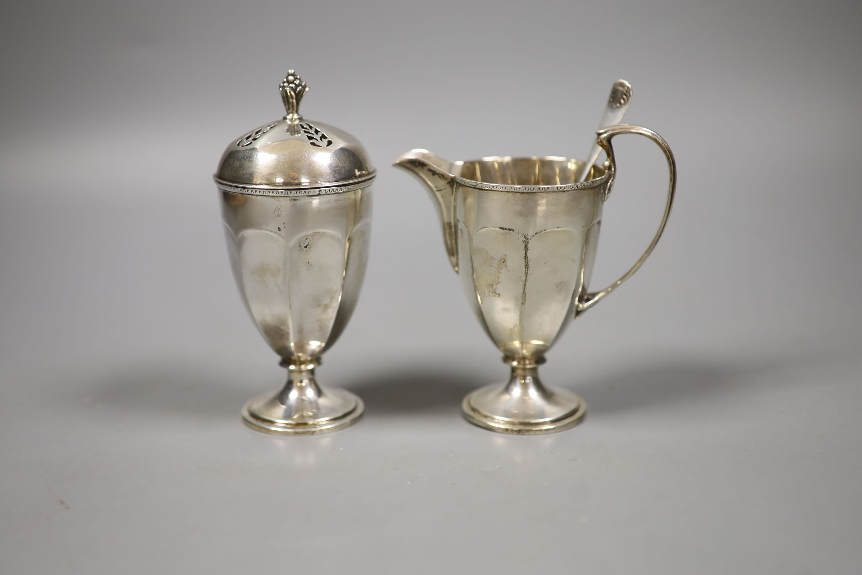 A George V silver helmet shaped cream jug, a silver sugar caster and a sifter spoon (3)